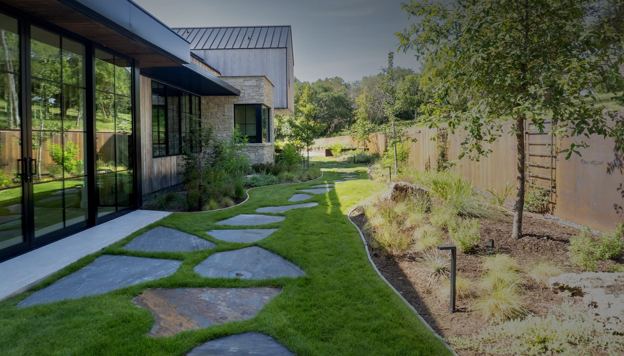 Custom landscape design with flagstone walkway, native plantings and modern home by Outdoor Living in Texas near Waco, TX